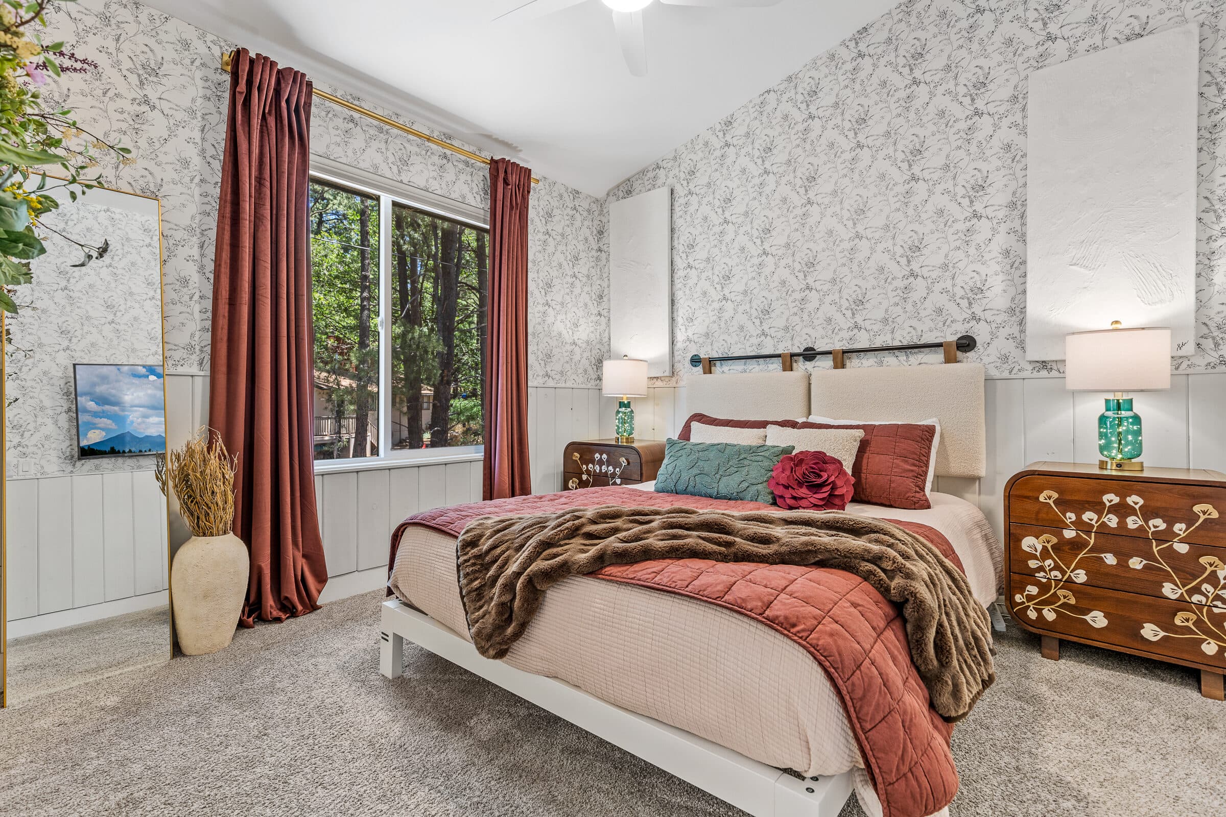 A guest bedroom dressed in warm tones with a forest-view window